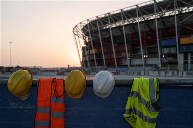 Stadium silhouette and worker safety gear suggesting Qatar World Cup labor reforms